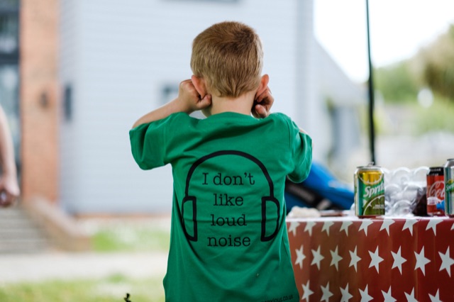 Boy wears green t shirt which says I Don't Like Loud Noise on the back with a headphone design